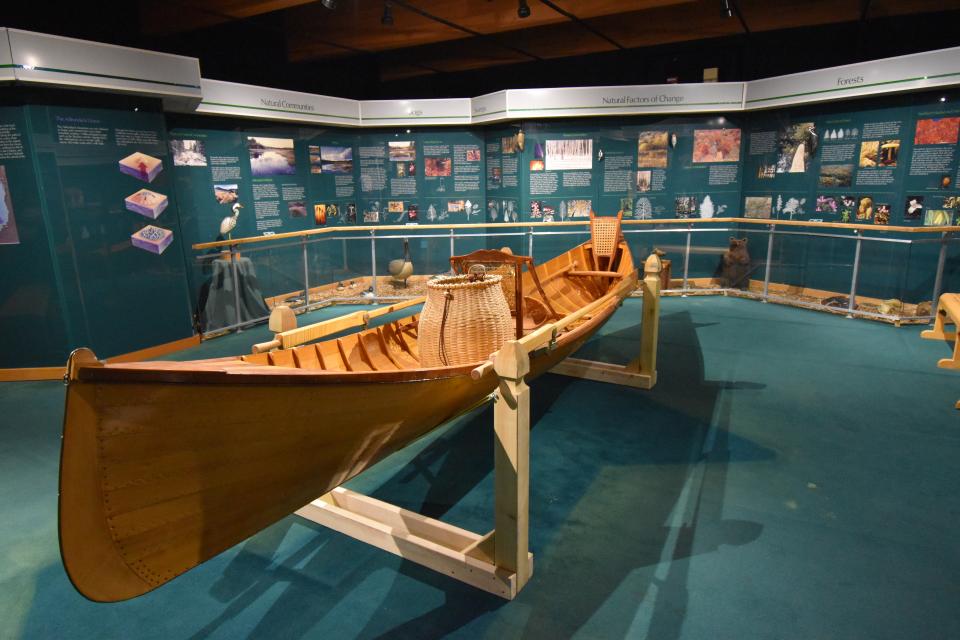 A beautiful, shiny Adirondack Guide Boat and packbasket in the middle of an interpretive display room with signs.
