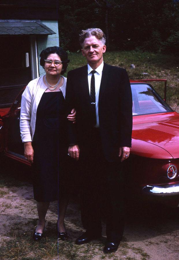 A man and a woman pose in front of a red car.