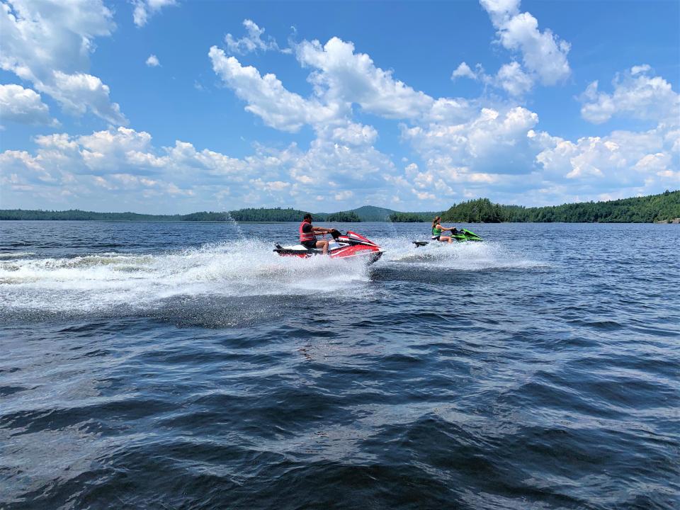 Two people riding jet skis on a sunny day. Mountains in the background.