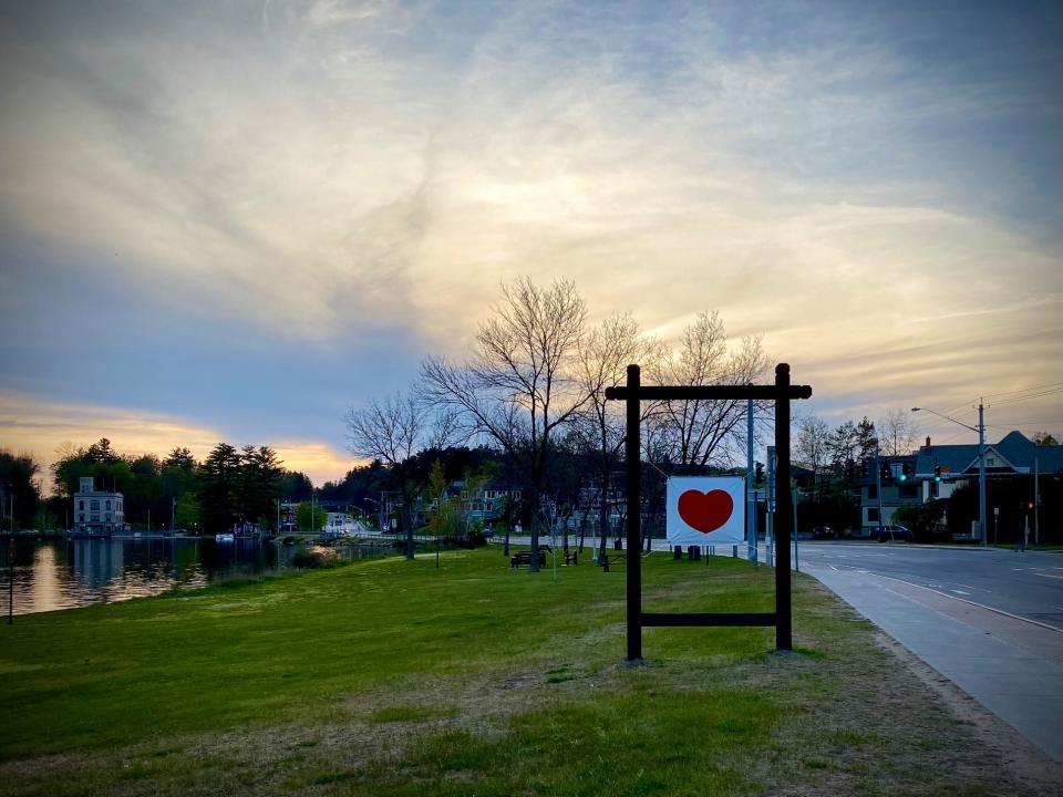 A poster with a red heart is displayed on a lawn with the sun setting in the background