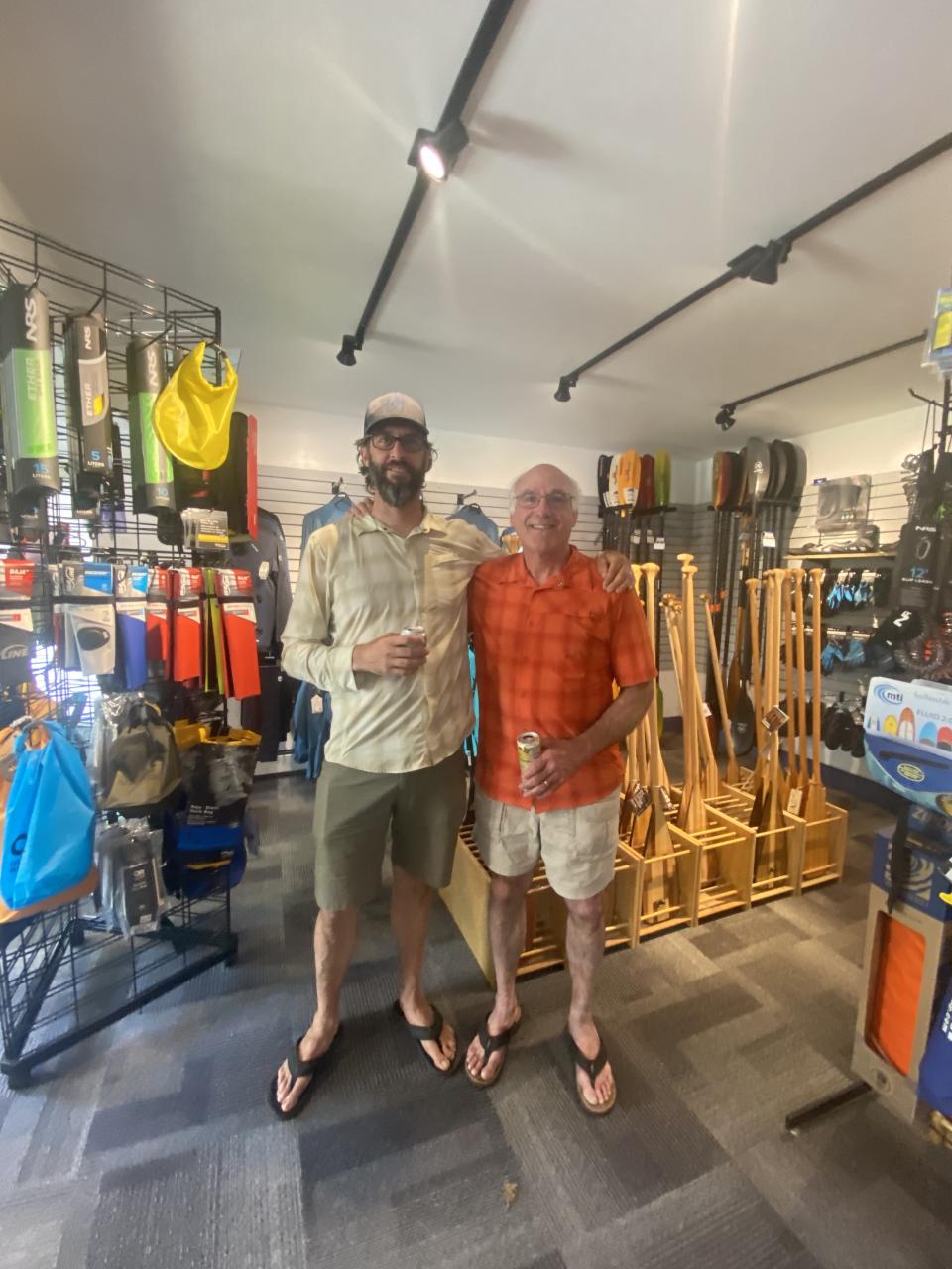 Two men stand inside a store in front of paddle gear