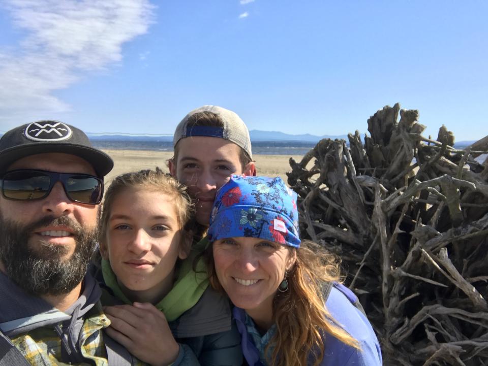 Jason Smith stands with his wife and two children on a beach with a large pile of driftwood behind them