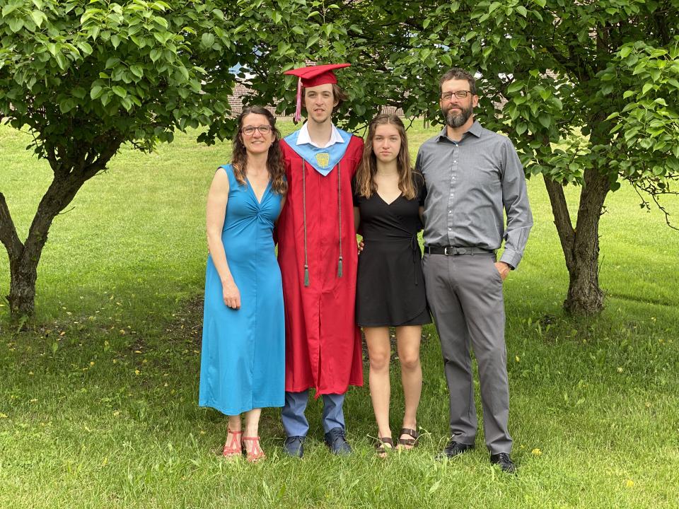 Jason Smith with his daughter, wife, and son on his son's graduation day. His son is wearing a red graduation cap and gown.