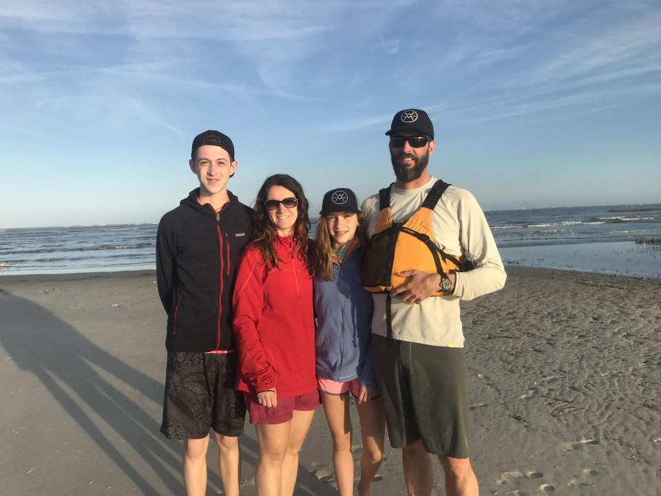 Jason Smith, his wife, and two teenage children stand on a beach with water behind them.