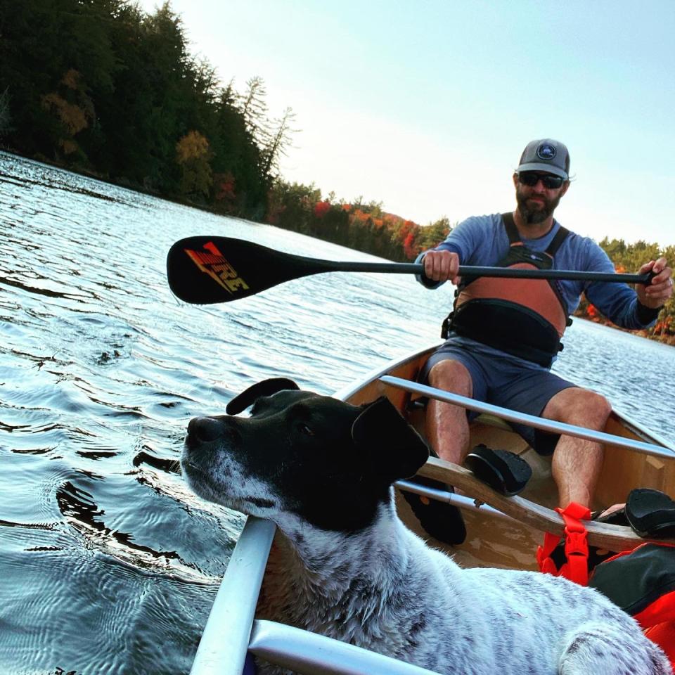 Jason smith paddling a lake in a canoe with fall foliage in the background