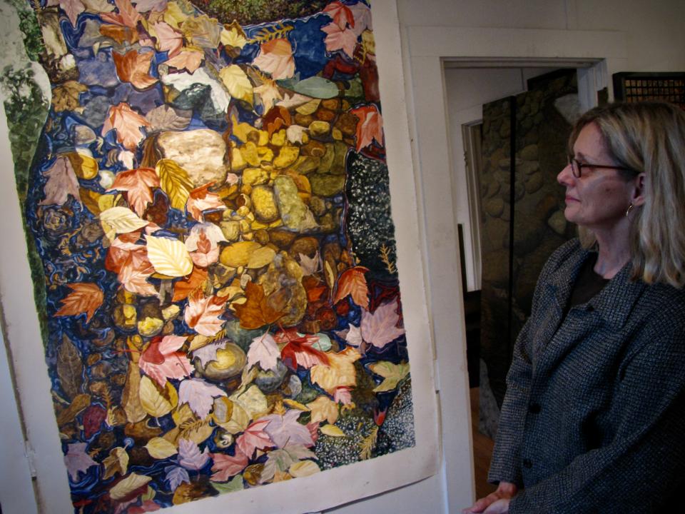 A woman stands in front of a large, realistic painting of leaves.