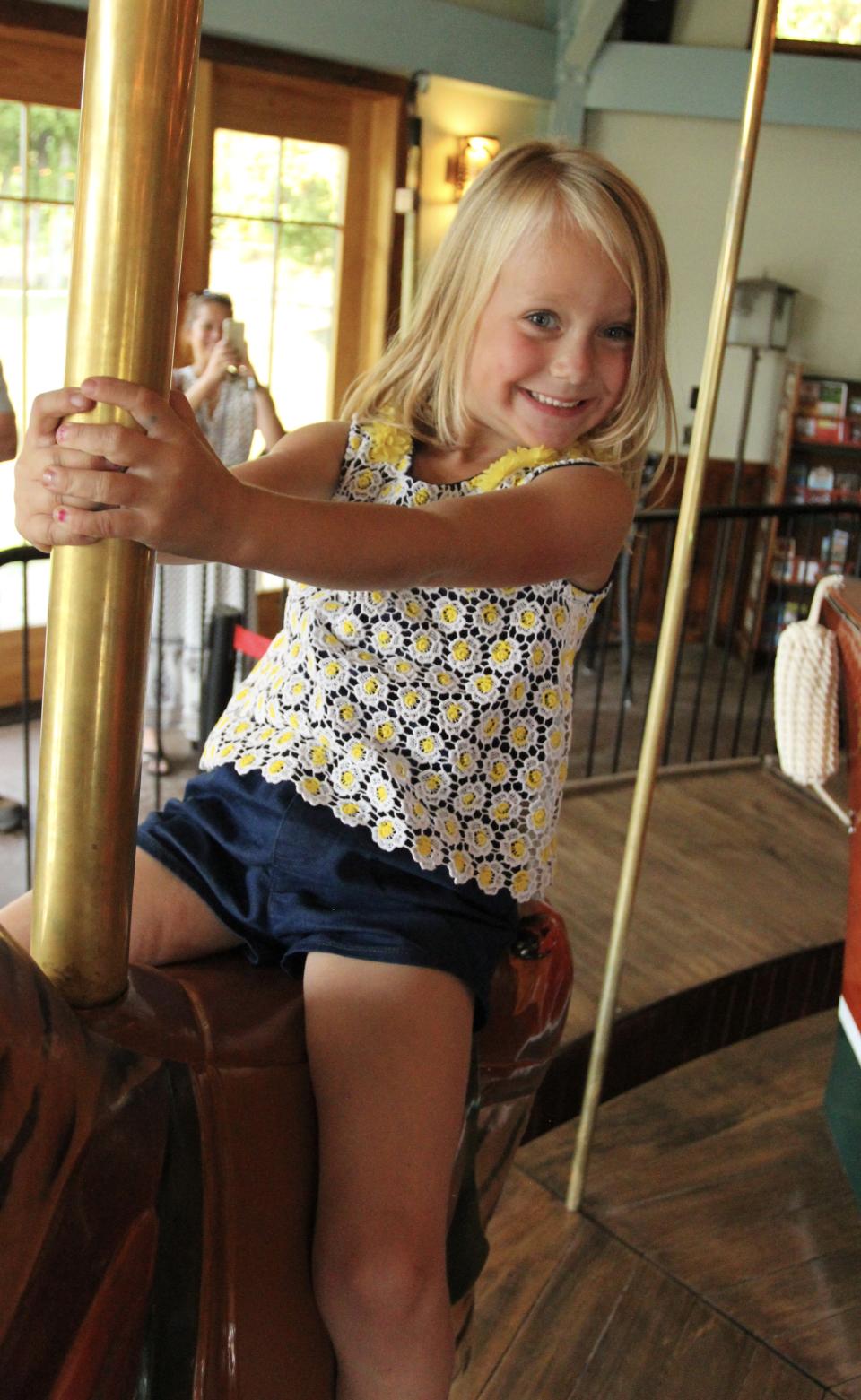 A blonde girl smiles while riding a carousel.