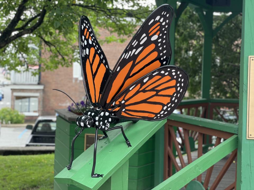 A large metal sculpture of a black, white, and orange butterfly on a railing.