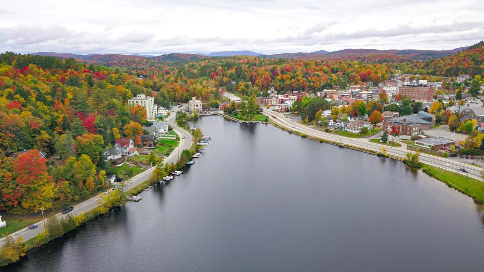 A aerial view of downtown Saranac Lake in the fall with distant mountains and buildings in the foreground.
