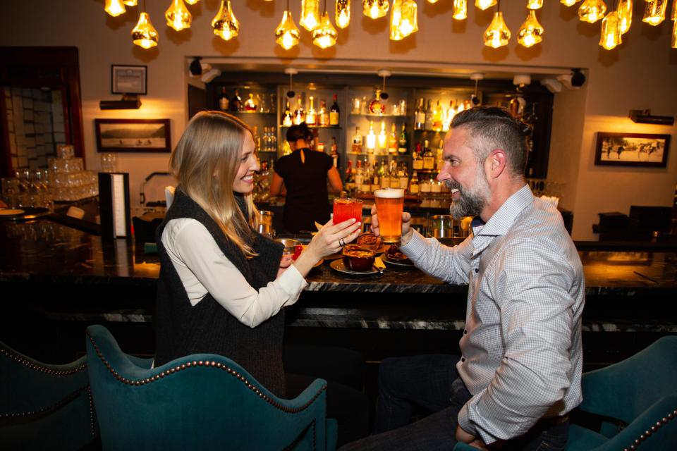A couple cheers'ing at the restored and historic Great Hall Bar at Hotel Saranac.