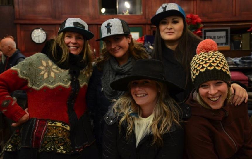 A group of women smiling wearing hats in a store.