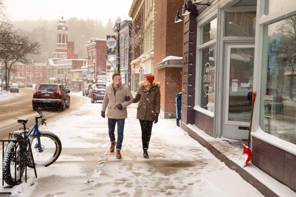A couple walking down a snowy street as the snow falls around them.