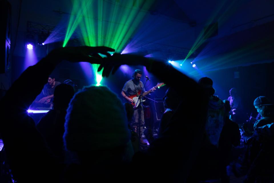 People dance in front of a band in a colorfully lit nightclub.