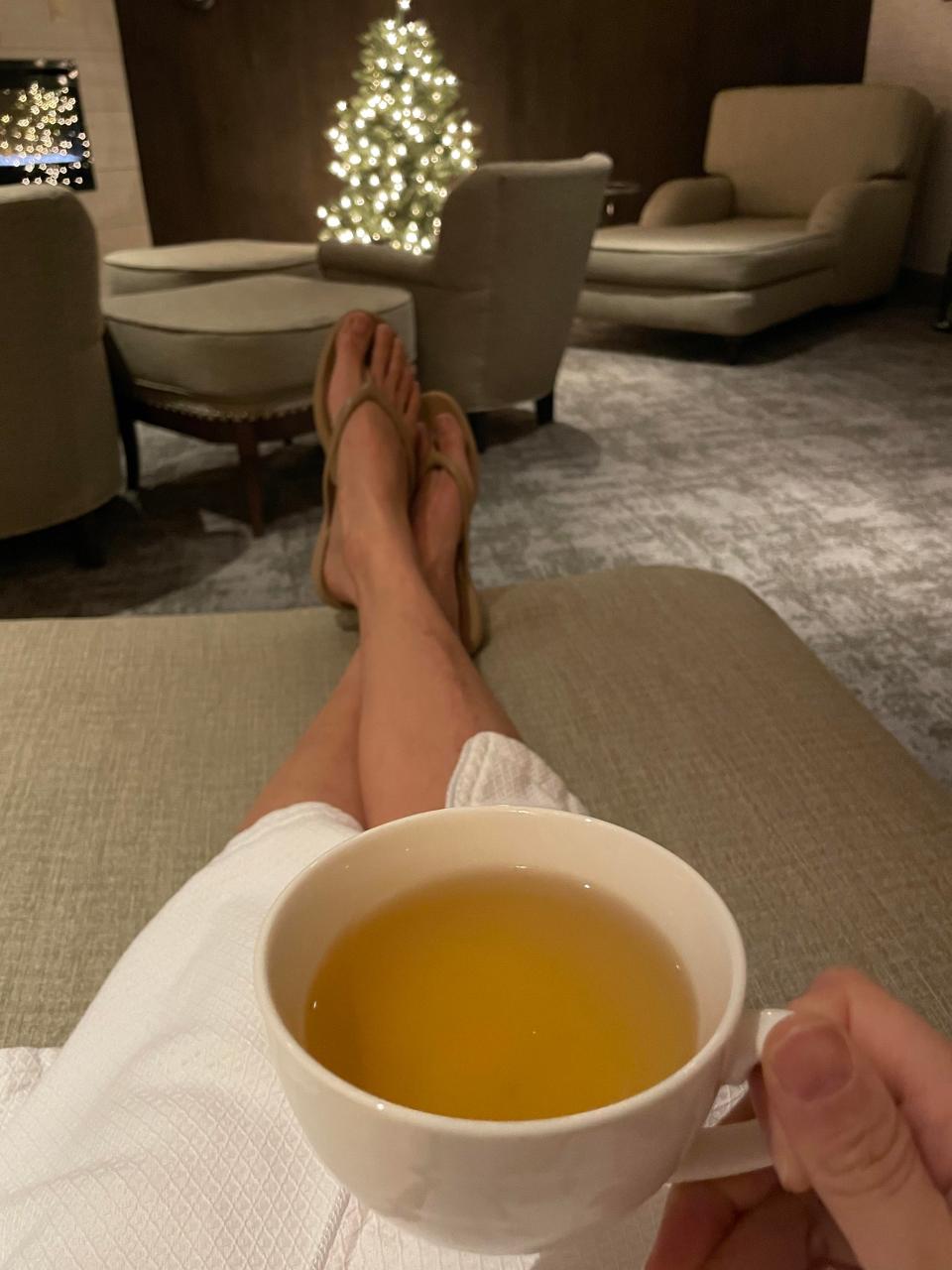 A woman lounges on a couch while wearing a spa robe and drinking a mug of tea