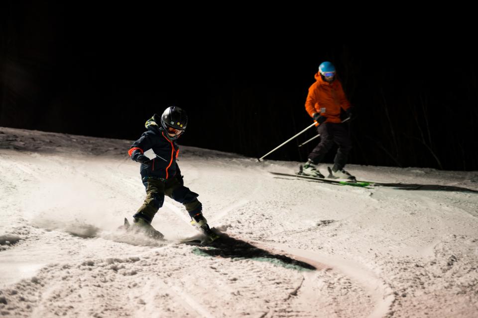 A father and son downhill ski under the night lights.