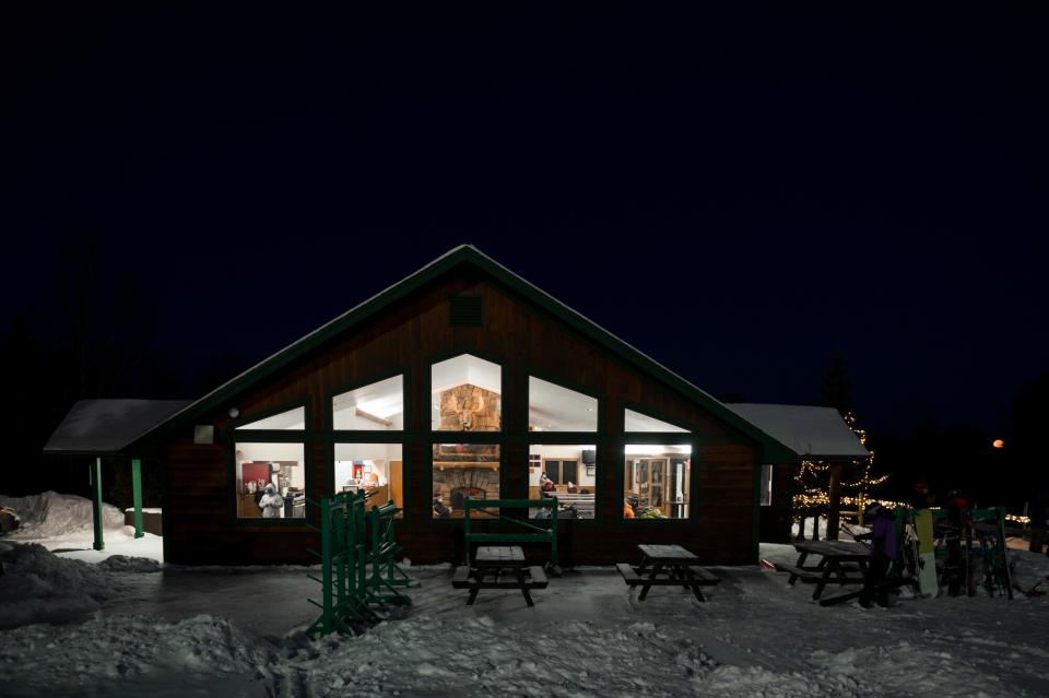 The ski lodge in the night but glowing from the inside with warm lights.