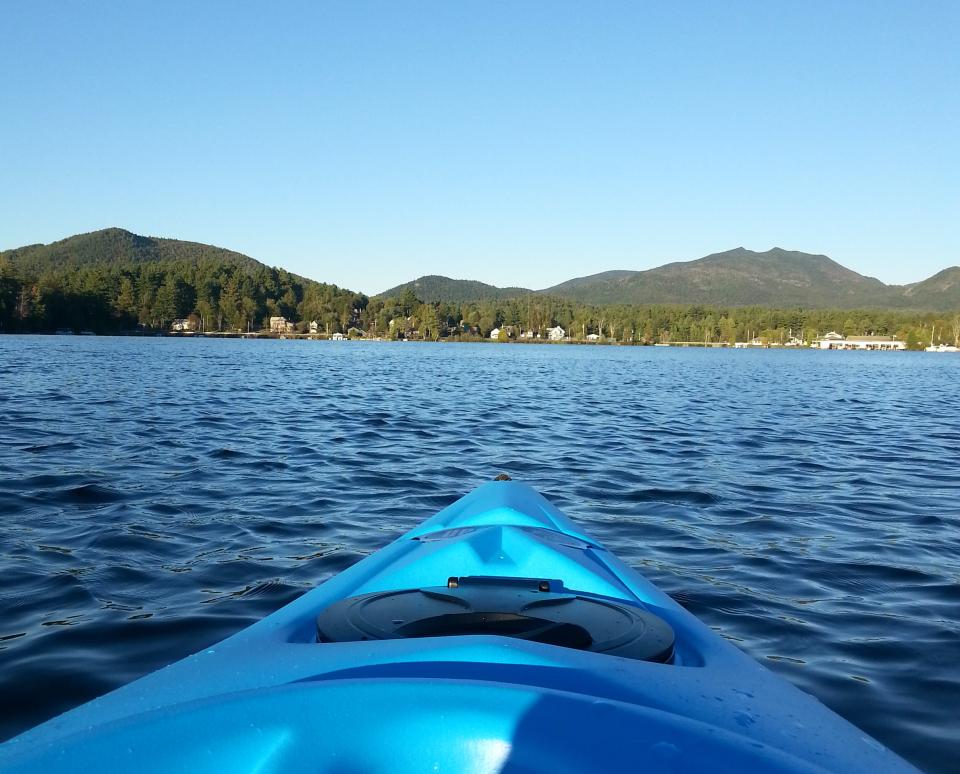 A blue kayak on the lake with multiple mountains in the background.