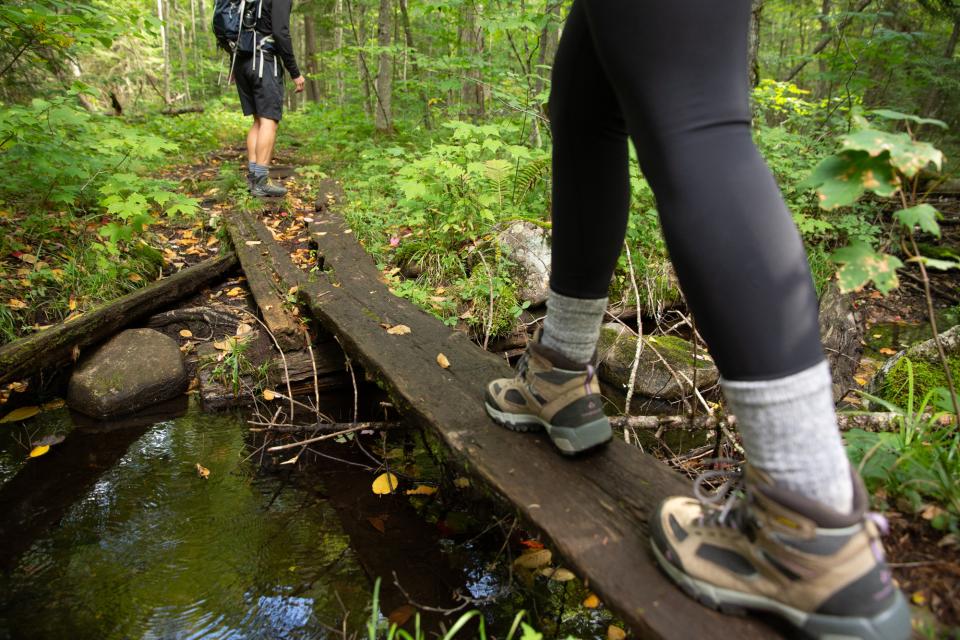 Two hikers cross a wooden bridge over a creek.