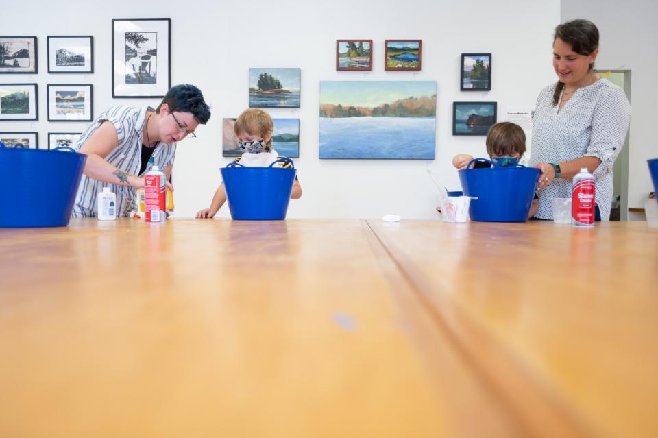 Two women oversee two small children completing art activities in a gallery.