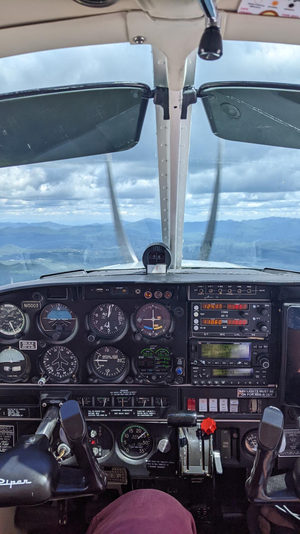 The view of airplane controls from the pilot's seat, with mountains beyond.