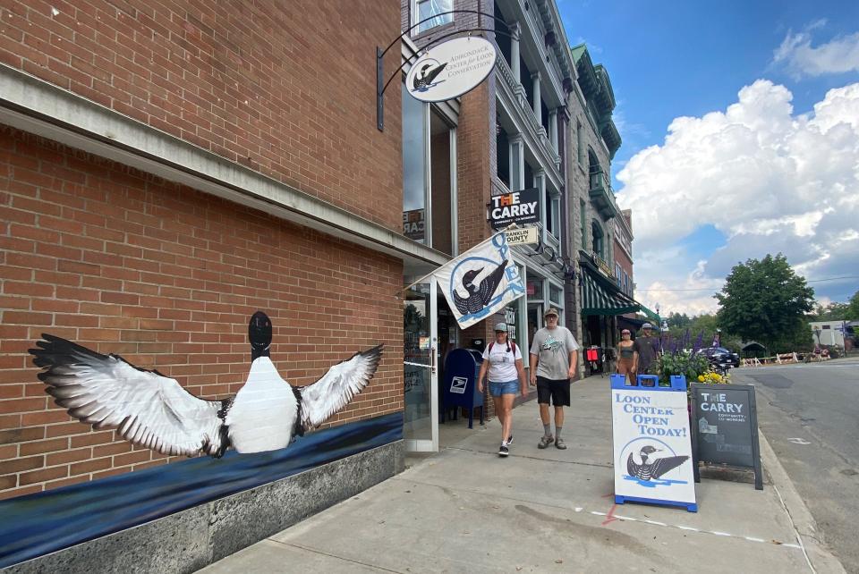 a couple walks past a loon mural on a clear day.