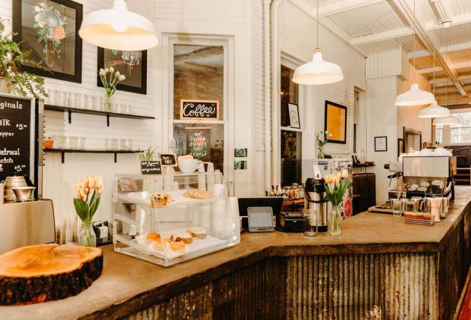 A coffee shop with a rustic bar with desserts and hot drink machines.