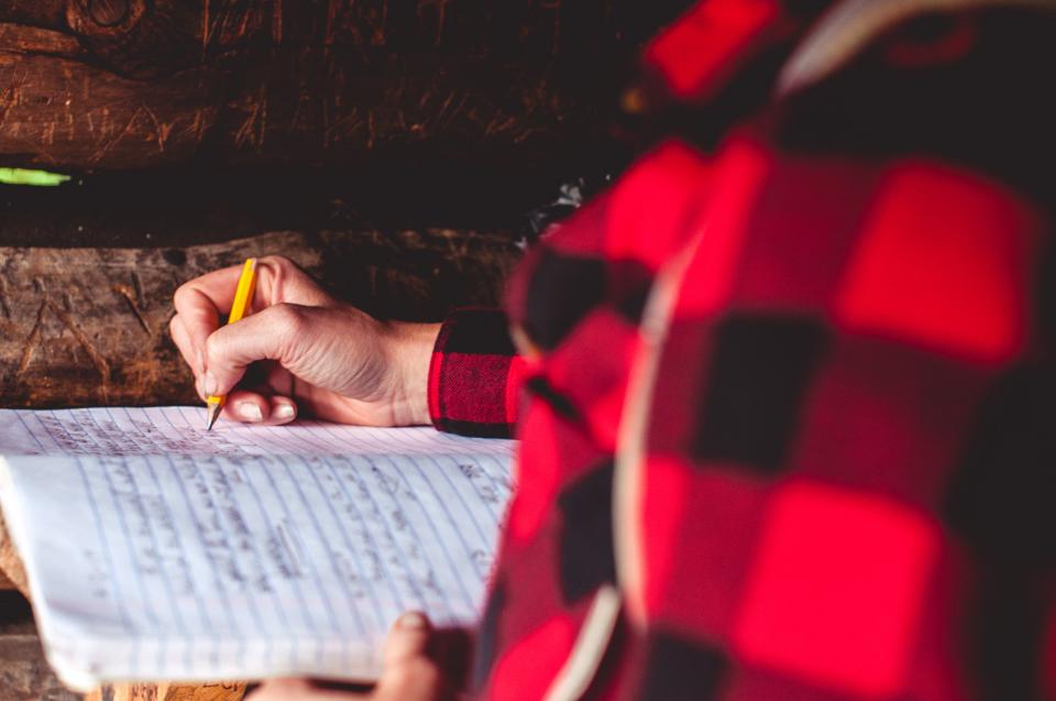 A person wearing a flannel writes in a notebook
