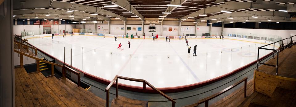 An ice rink as viewed from the bleachers. People are skating on the ice.