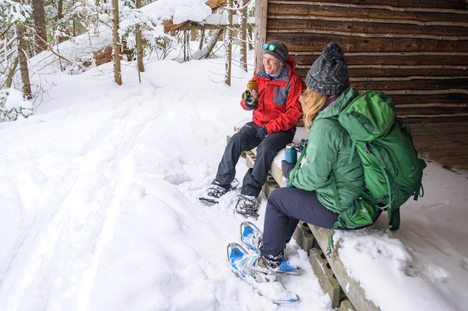 Two friends take a break from snowshoeing and enjoy a drink of water in a lean to in a snow covered forest