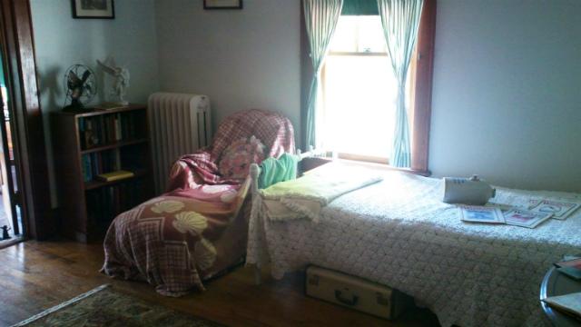 The bedroom of one of the cure cottages of Saranac Lake, complete with a bed, recliner, and ceramic jug used to keep feet warm at night known as a "pig"