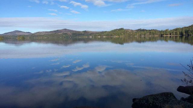 View from the shore along the Floodwood canoe route with mountains in the background and the reflection of blue skies and white clouds in the flat water