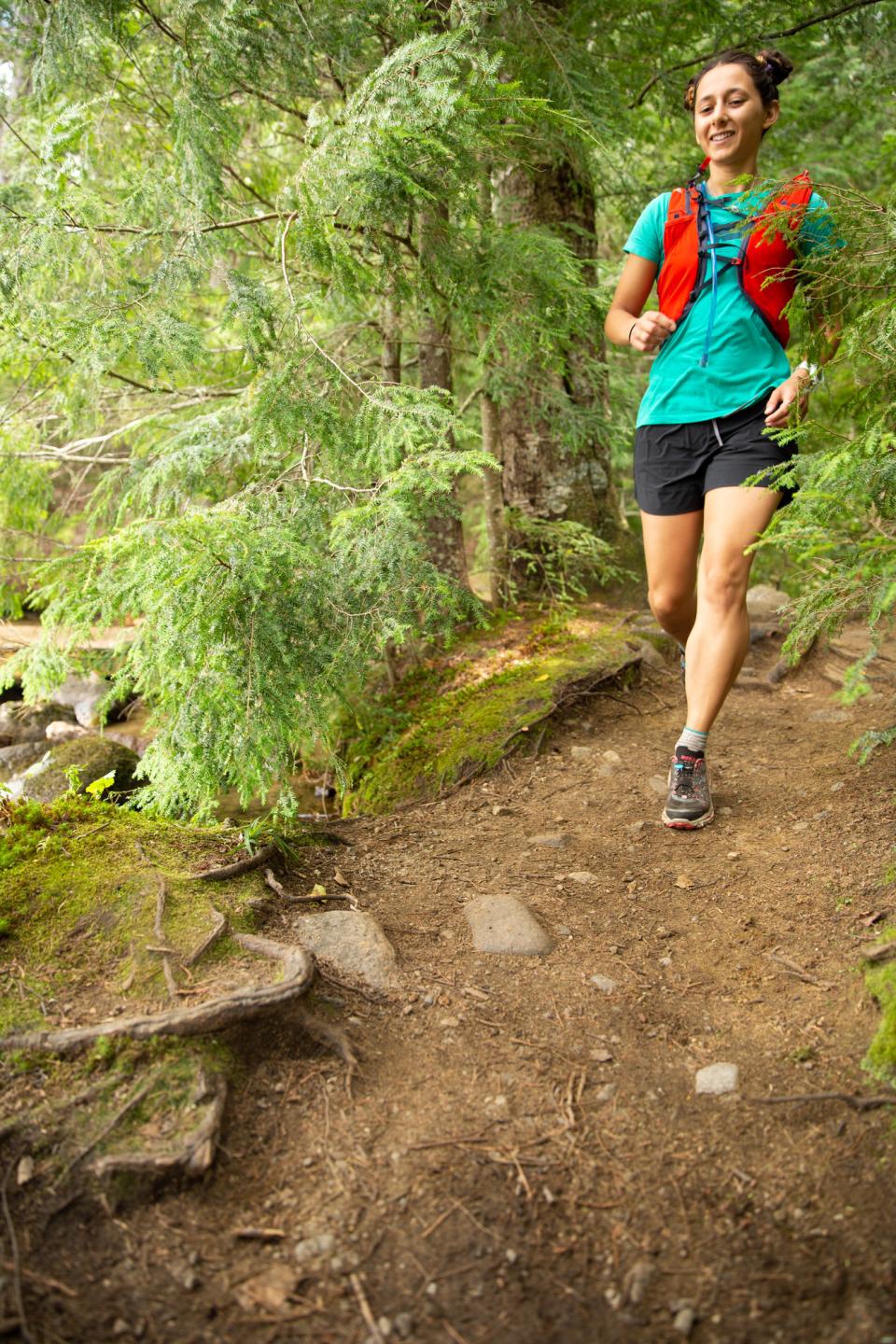 A young woman in sportwear runs a wooded trail in the Adirondacks.