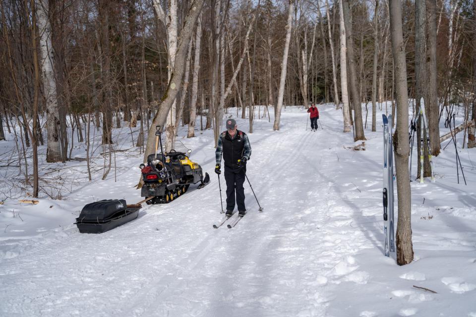 A skier passes a snowmobile on a snowy trail