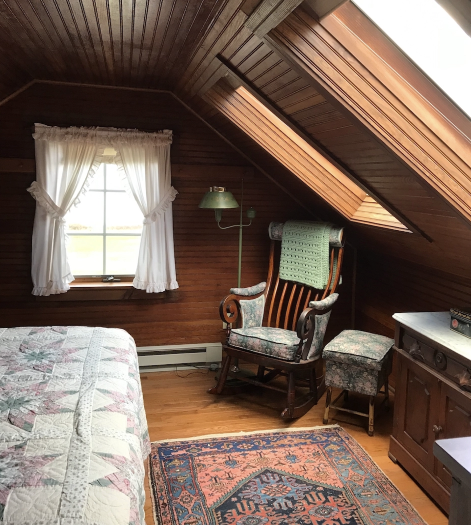 A cozy, beadboard paneled farmhouse bedroom with skylights and antique furniture.
