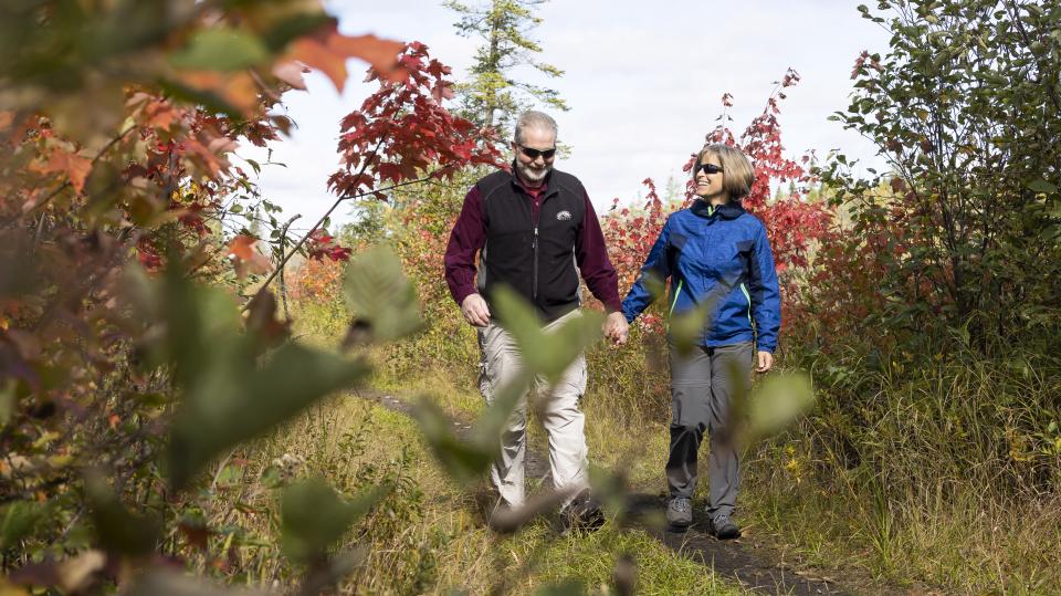 Two older hikers walk on a trail surrounded by fall foliage