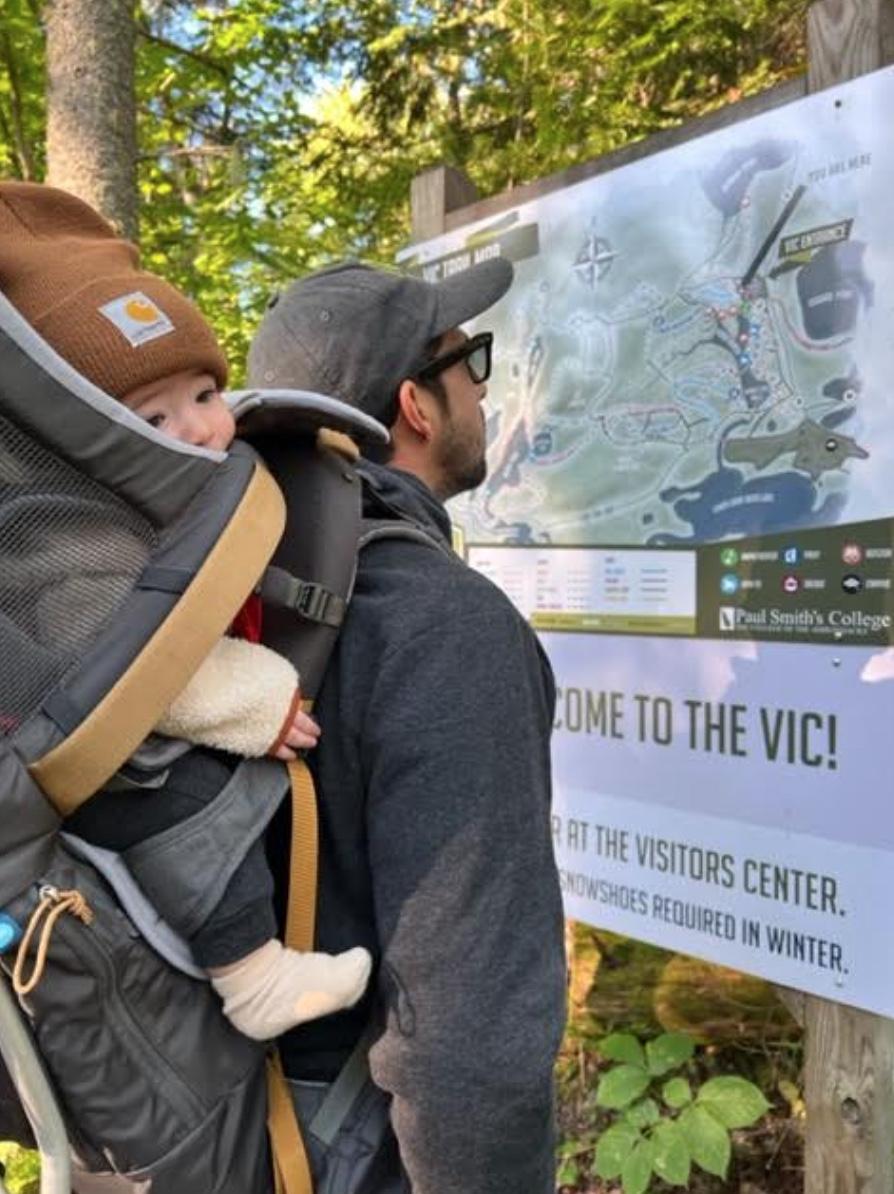A hiker and his baby look at a map for a trail system
