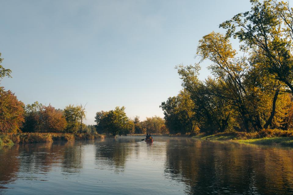 Paddlers in a canoe float down a fall morning.