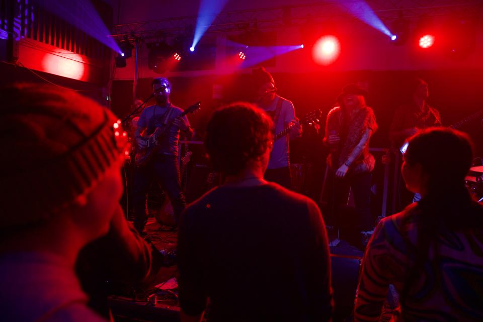 A crowd watches a band play in a red-lit event space.