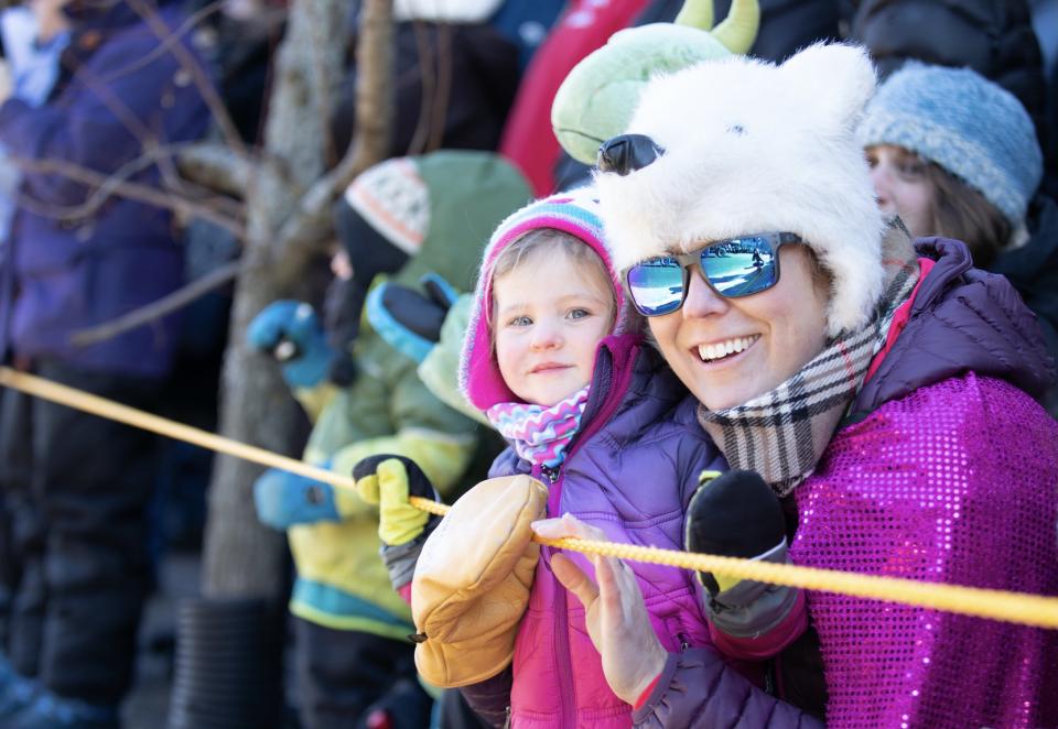 A woman wears sunglasses and a polar bear hat as she smiles with a young child.