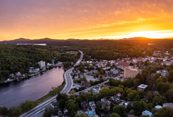 Aerial view of Saranac lake with a warm orange and pink sunset at the backdrop.