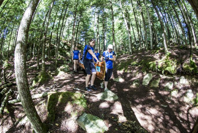 A team of women in matching blue shirts carry a beautiful wooden canoe on a dirt path through the woods to the next launching point in the Adirondack 90-Miler