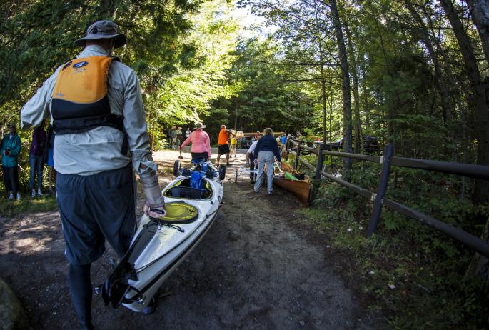 Groups of racers carrying their kayaks and canoes towards the next launching point of the Adirondack Canoe Classic