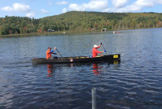 Two men paddle a black canoe across a lake during the Adirondack 90-Miler