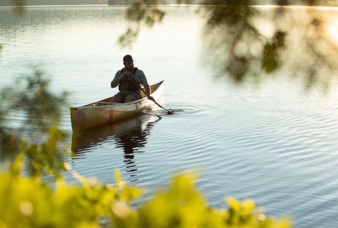 Photograph of a man paddling along a peaceful lake in a canoe