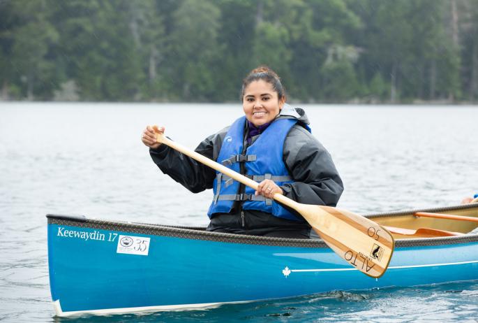 Woman smiling while holding an oar as she sites in the front of a canoe rental from a Saranac Lake outfitter