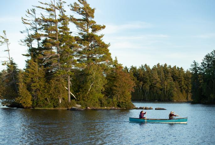 Two women paddle a blue canoe in one Saranac Lake's secluded waterways