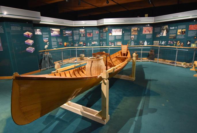 A beautiful, shiny Adirondack Guide Boat and packbasket in the middle of an interpretive display room with signs.