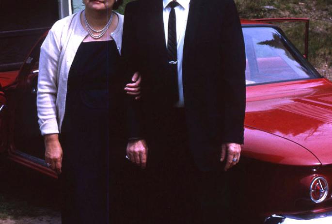 A man and a woman pose in front of a red car.