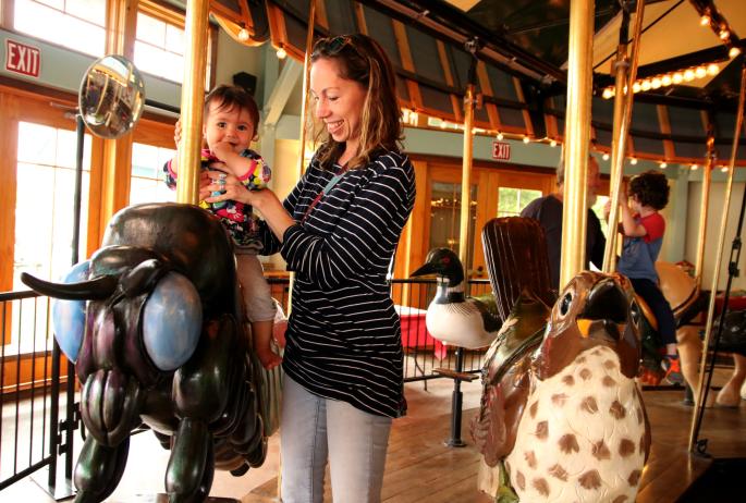 Woman holds a small child on a carousel animal