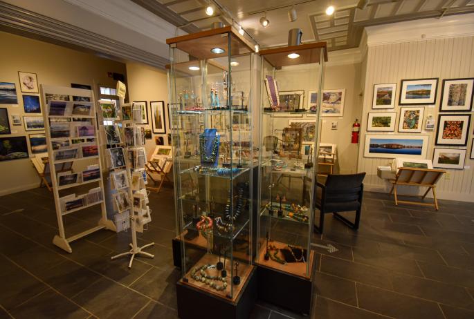 Displays at an art gallery: jewelry, paintings, photographs, and post cards.